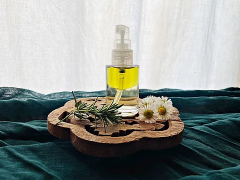 eine Holzscheibe. darauf ein Rosmarinzweig, Gänseblümchen und eine Pumpflasche mit Öl