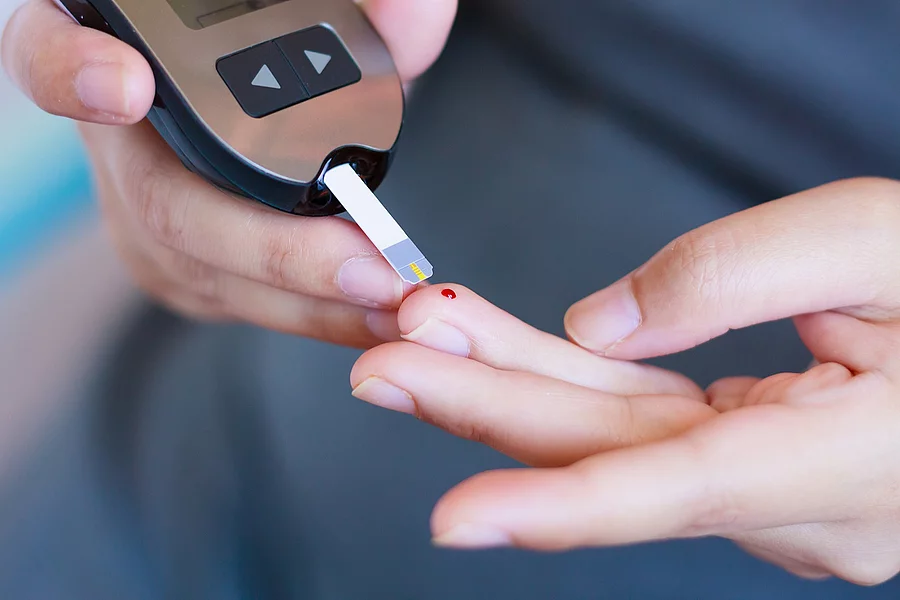 Mann testet seinen Blutzucker mit einem Teststreifen und Tropfen Blut am Finger