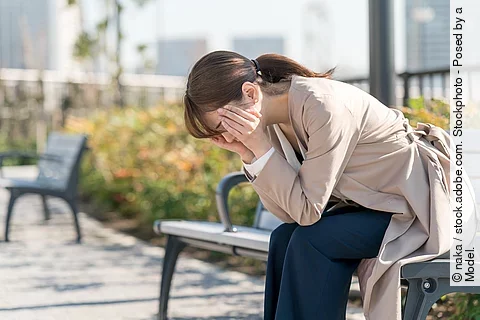 Frau sitzt erschöpft auf einer Bank, den Kopf in den Händen