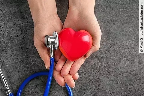 Hände halten ein Stethoskop und eine Herzfigur. 