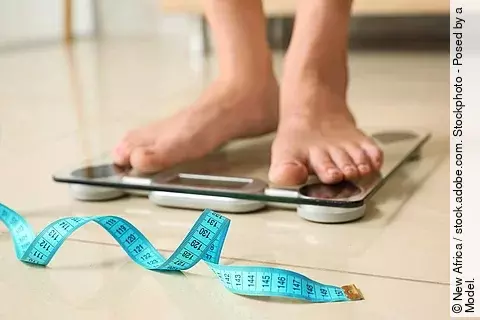 Füße auf einer Personenwaage, davor liegt ein Maßband