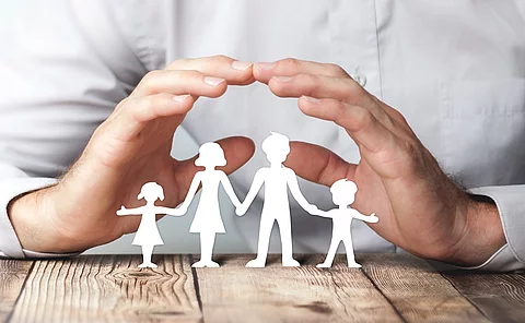 Schützende Hände über einer Familie aus Papier