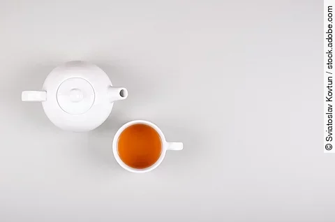 Eine weiße Teekanne mit Teetasse vor hellem Hintergrund