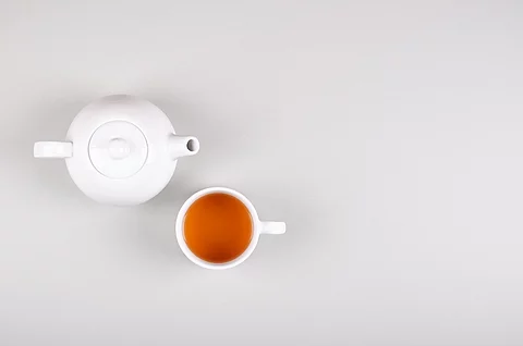 Eine weiße Teekanne mit Teetasse vor hellem Hintergrund