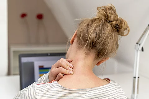 Frau am Laptop massiert sich den Nacken