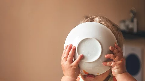 Kleinkind, das hungrig den Teller vor das Gesicht hält und ableckt.