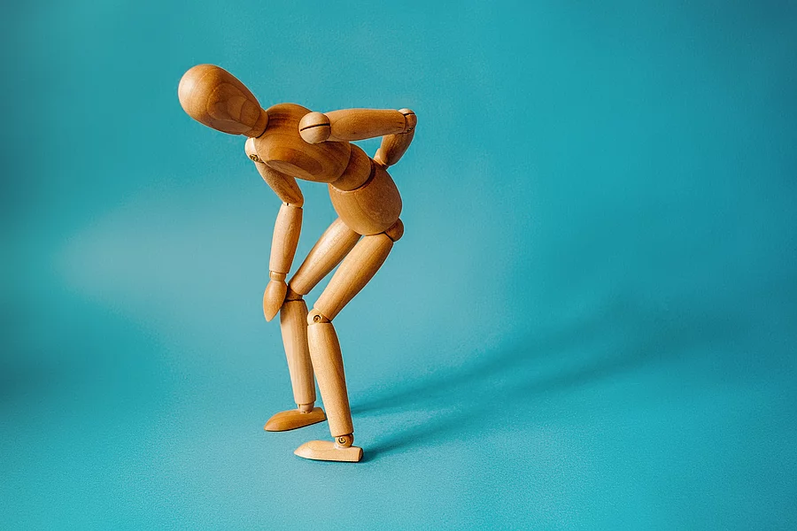 Concept of back pain. A wooden figure depicts a pain in the back Holzfigur steht gekrümmt und hält sich den Rücken
