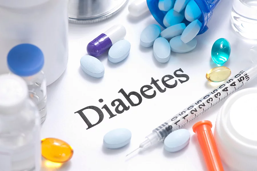 Schriftzug Diabetes, darum herum liegen bunte Pillen, Spritze