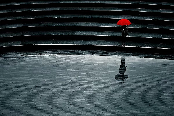 Mensch mit rotem Schirm bei Regen allein auf einer Treppe, Einsamkeit