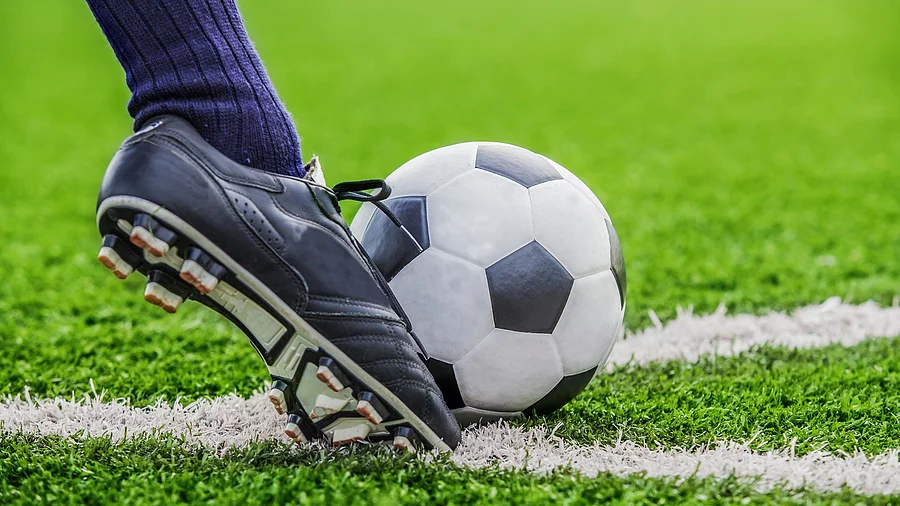 Unterschenkel mit Fußballsocken und Fußballschuh kickt den Ball auf Rasen