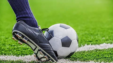 Unterschenkel mit Fußballsocken und Fußballschuh kickt den Ball auf Rasen Fußball mit Fuß auf dem Fußballfeld