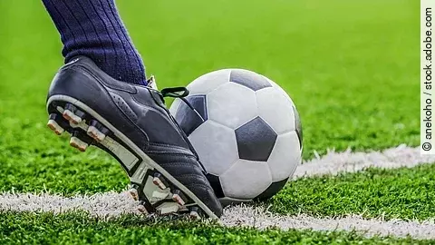 Unterschenkel mit Fußballsocken und Fußballschuh kickt den Ball auf Rasen