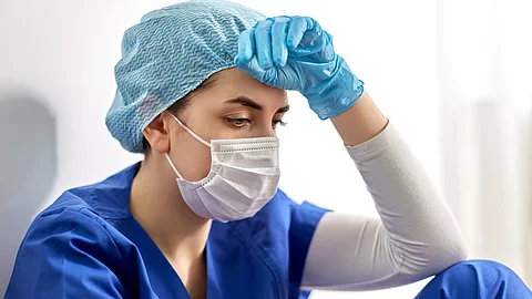 sad doctor or nurse in protective face mask junge Ärztin mit Mundschutz in OP-Kleidung; Symbolbild psychische Belastung während der Corona-Pandemie