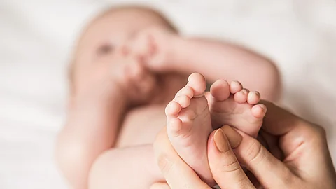 Mutter hält die Füßchen eines liegenden Babys