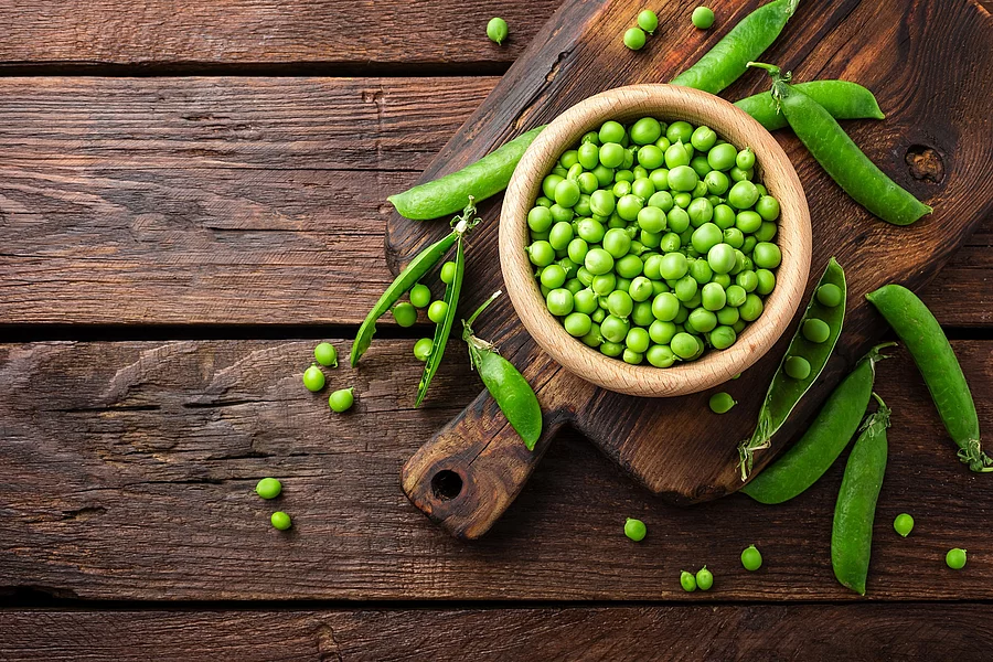 Green peas Erbsenschoten und Erbsen in einer Schüssel auf dunklem Holztisch