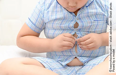 Kind mit Übergewicht, welches sein Hemd nicht schließen kann. 