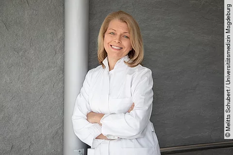 Porträtfoto: Prof. Ute Seeland lehnt im weißen Kittel an Betonsäule