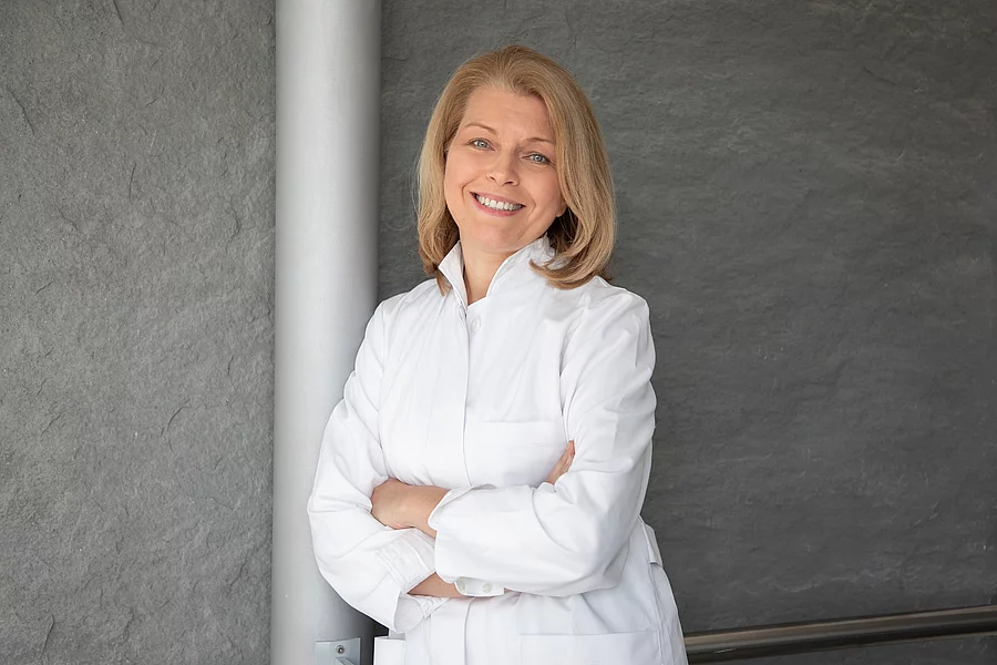 Porträtfoto: Prof. Ute Seeland lehnt im weißen Kittel an Betonsäule