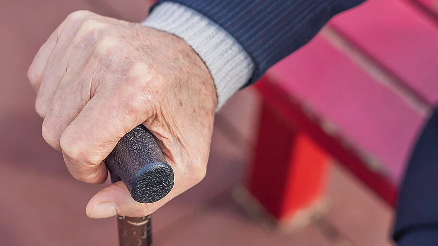 Hand einer Seniorin auf einen Stock gestützt