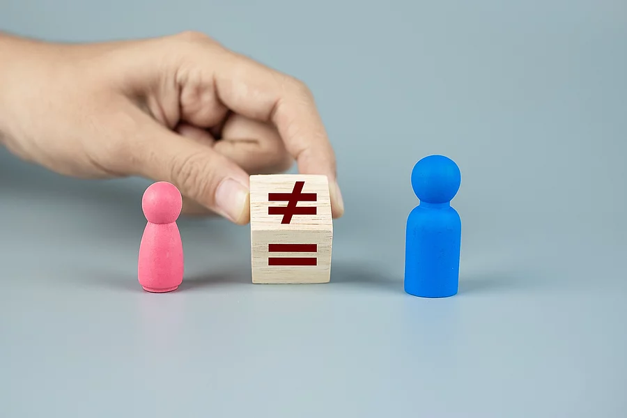 Pinke und blaue Spielfigur zwischen denen ein Holzwürfel, mit dem Ungleich-Zeichen, von einer Hand festgehalten wird. 