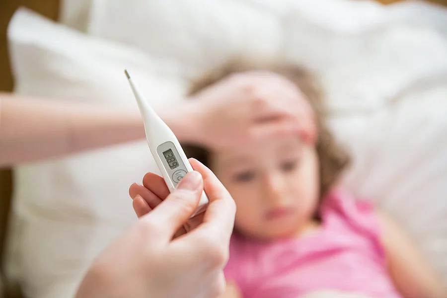 Kleines Mädchen im Bett, Mutter misst Fieber