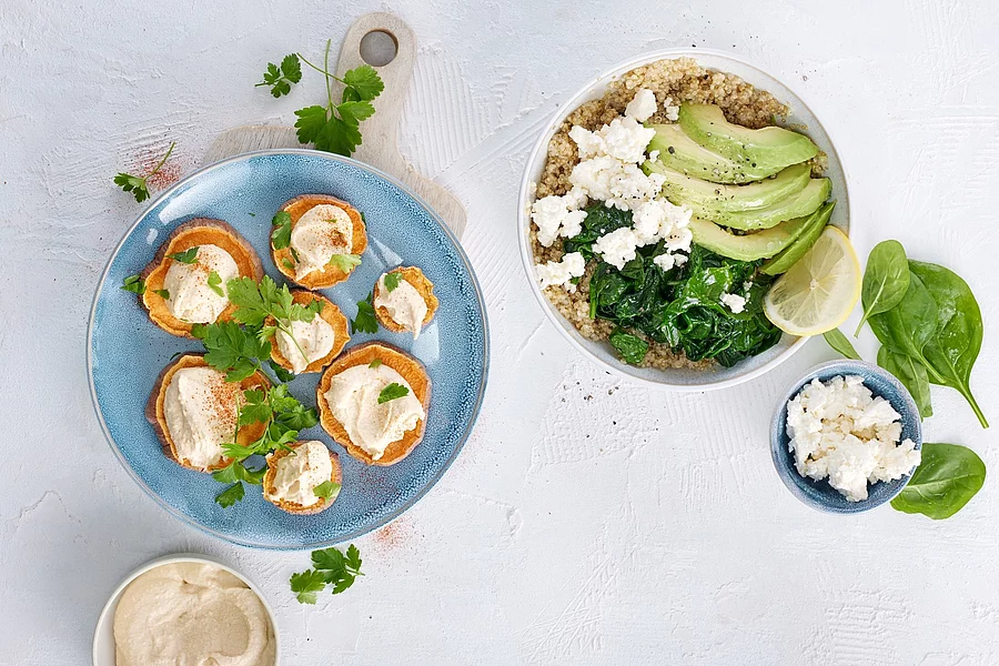 Ballaststoffreiche Speisen auf Tellern: Hummus, Süßkartoffel, Quinoa mit Spinat, Melone und Schafskäse