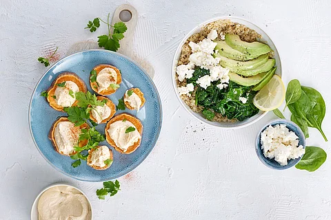 Ballaststoffreiche Speisen auf Tellern: Hummus, Süßkartoffel, Quinoa mit Spinat, Melone und Schafskäse