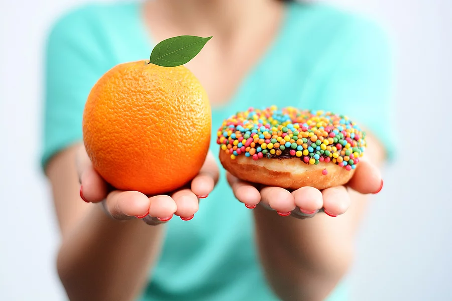 Abwägen: Junge Frau hält Orange in der einen, Donut in der anderen Hand 