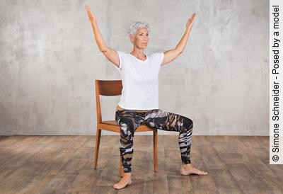Frau im mittleren Alter praktiziert Yoga auf einem Stuhl aus Holz.