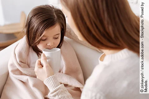 Mutter gibt kleinem Mädchen, das im Bett sitzt, etwas zu trinken