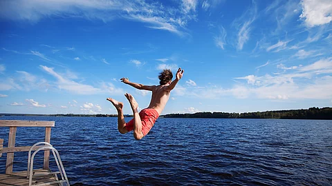 Junger Mann springt von einem Deck in einen See Junger Mann springt von einem Deck in einen See
