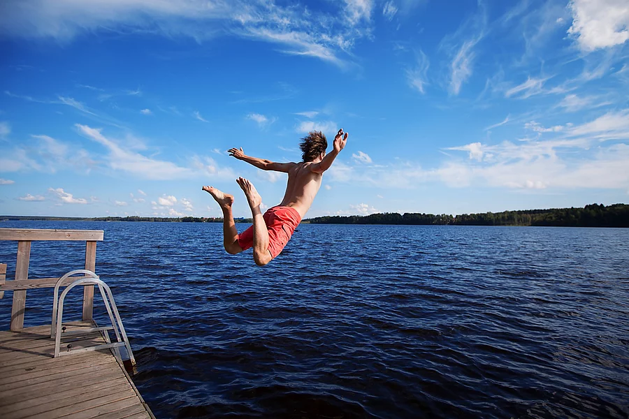 Junger Mann springt von einem Deck in einen See