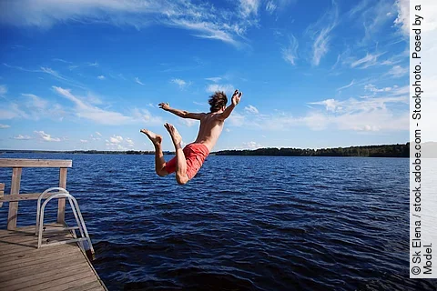 Junger Mann springt von einem Deck in einen See