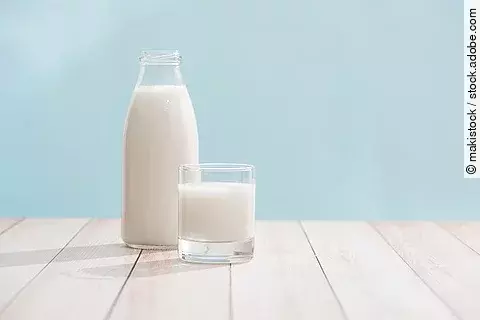 Eine Flasche und ein Glas gefüllt mit Milch stehen auf einem Tisch. 