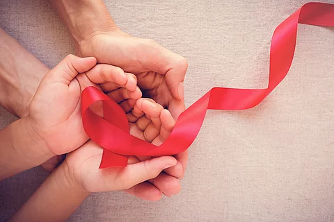 4 Hände halten eine rote AIDS-Schleife