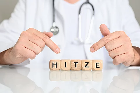 Arzt zeigt auf Holzklötzchen mit den Buchstaben HITZE