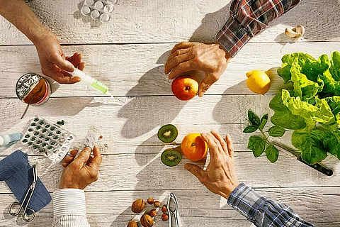 4 Hände mit Tabletten, Mandarinen, Spritzen und Nüssen.