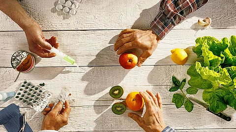 4 Hände mit Tabletten, Mandarinen, Spritzen und Nüssen.