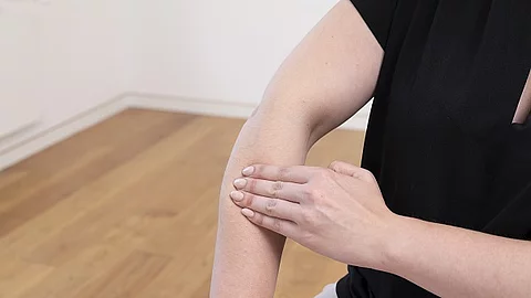 Frau in schwarzem T-Shirt, die sich auf den Unterarm mit der anderen Hand drückt.