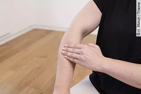 Frau in schwarzem T-Shirt, die sich auf den Unterarm mit der anderen Hand drückt.