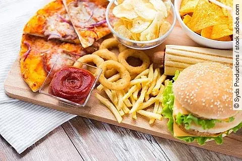 Fast Food auf einem Tisch: Burger, Pommes, Zwiebelringe, Pizza.