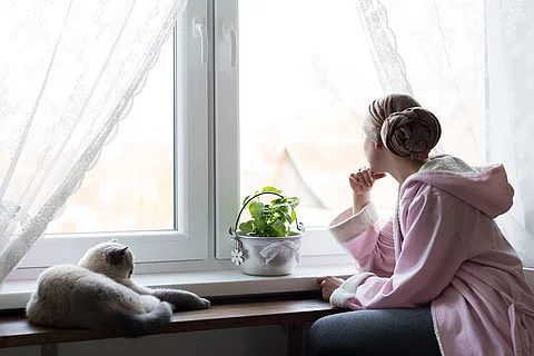 Junge Frau, Krebspatientin sitzt am Fenster