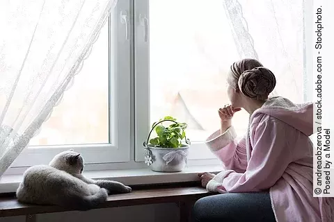 Junge Frau, Krebspatientin sitzt am Fenster