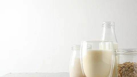 Glasflasche und Glas mit Milch, daneben Haferflocken und Mandeln