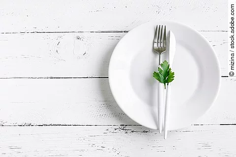 Fasten: weißer leerer Teller mit Messer, Gabel auf weißem Holzuntergrund