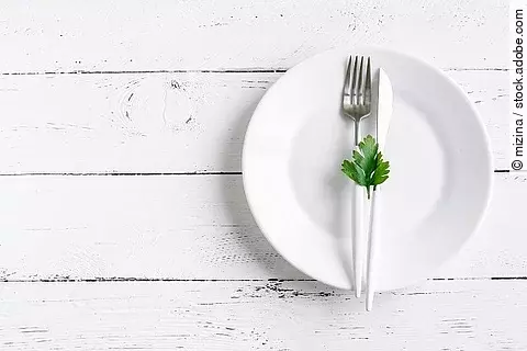 Fasten: weißer leerer Teller mit Messer, Gabel auf weißem Holzuntergrund