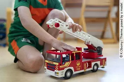 Kind spielt mit einem Spielzeug-Feuerwehrauto. 