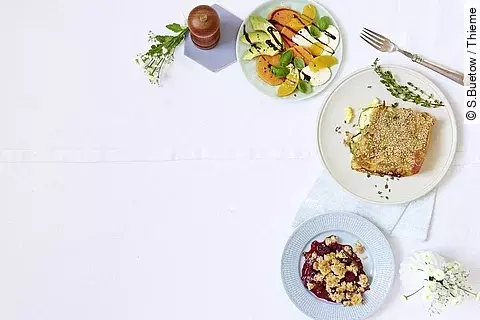 Drei Teller mit verschiedenen Gerichten, Besteck und Pfeffermühle rechts außen im Bild platziert. 