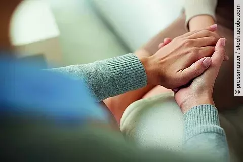 Eine Frau in einem türkisfarbenen Pullover hält die Hand eines anderen Menschen.