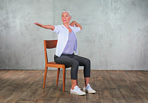 Frau im mittleren Alter praktiziert Yoga auf einem Stuhl aus Holz.